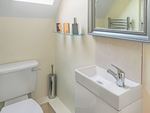 Ein Badezimmer mit Toilette, Waschbecken, Spiegel und einer Glasablage für Pflegeprodukte.