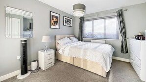 A bedroom with a bed, bedside table, lamp, dresser, window with curtains, and a radiator. - 3 bedroom accommodation in Rhyl (Rhyl)