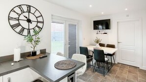 A modern kitchen with a large clock, dining table, chairs, and a TV mounted on the wall. - 3 bedroom accommodation in Rhyl (Rhyl)