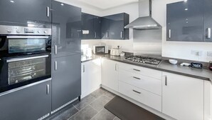 A modern kitchen with dark cabinets, a built-in oven, a microwave, a gas stove, and a digital clock. - 3 bedroom accommodation in Rhyl (Rhyl)