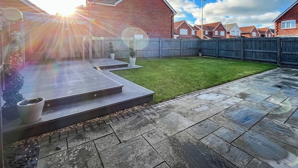 A residential backyard with a paved patio, a grassy lawn, and a wooden fence. - 3 bedroom accommodation in Rhyl (Rhyl)