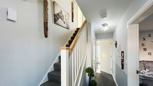 A hallway with a staircase, a small plant, and a door with Roman numerals on the wall. - 3 bedroom accommodation in Rhyl (Rhyl)
