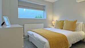 Ein Schlafzimmer mit Bett, Nachttisch, Lampe, Fenster, Heizkörper und einem Bilderrahmen.