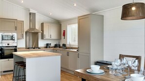 A modern kitchen with a central island, bar stools, a dining table set for four, and a hanging light fixture. - 2 bedroom accommodation in Chadwick, near Worcester (Chadwick, near Worcester)