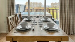 A dining table set for four with white plates, bowls, and glasses, overlooking a hot tub and a wooden deck. - 2 bedroom accommodation in Chadwick, near Worcester (Chadwick, near Worcester)