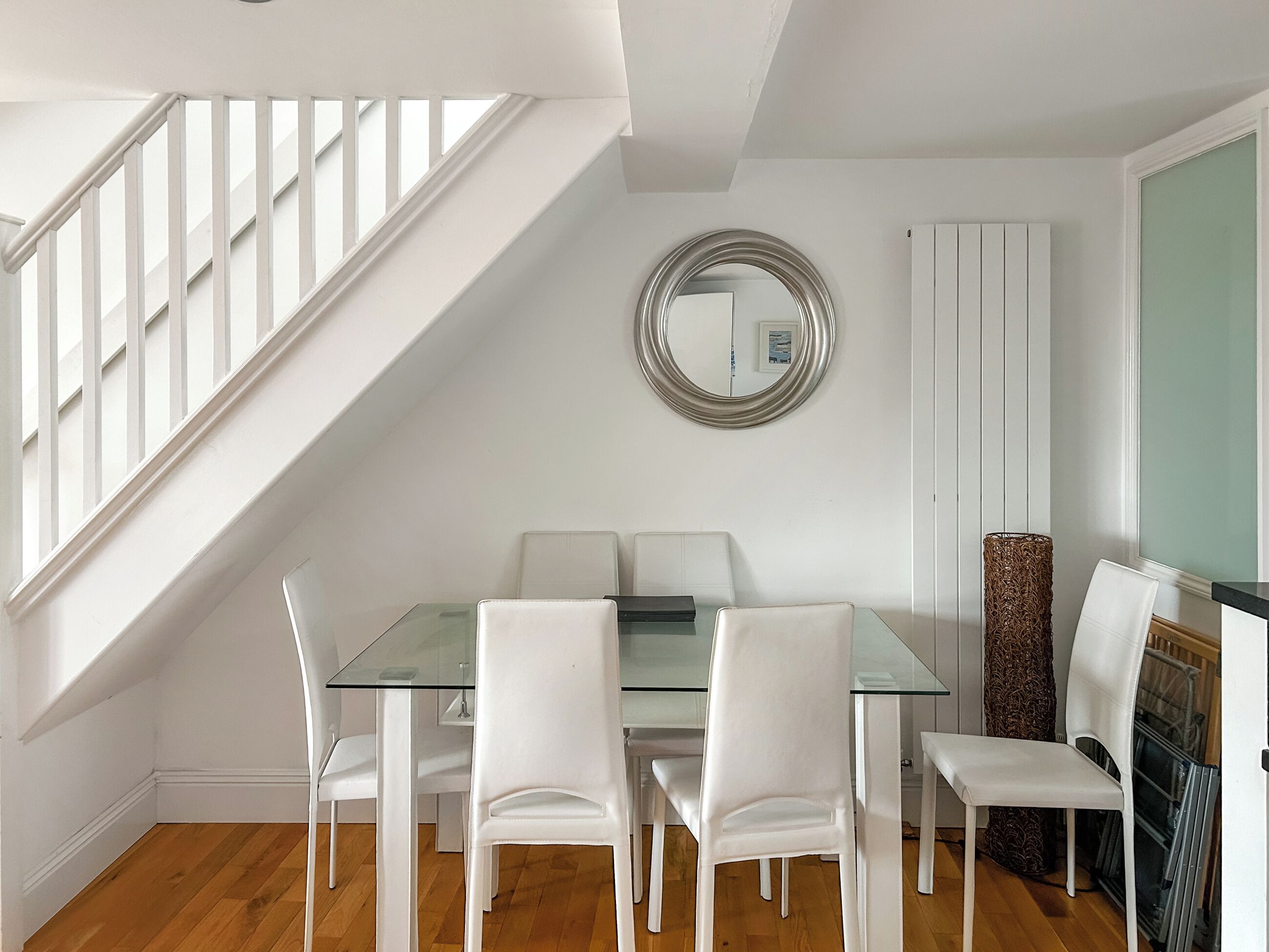 A dining area with a glass table, white chairs, a mirror, and a staircase.