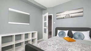 Een slaapkamer met een bed, een witte console tafel, een grijs hoofdeinde en een schilderij aan de muur.