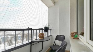 Een balkon met een kleintje tafeltje, twee stoelen, een potplant en een decoratief object.