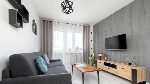 Een moderne woonkamer met een grijze bank, een houten salontafel en een televisie aan een grijze muur.