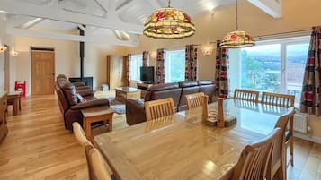 A spacious living area with a wooden dining table, leather sofas, and a large window offering a view.