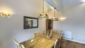 Un comedor con una mesa de madera, seis sillas, lámparas de vidrio emplomado colgantes, un espejo y un aparador con puertas de vidrio.