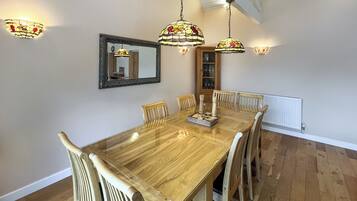 A dining area with a wooden table, six chairs, hanging stained glass lamps, a mirror, and a cabinet with glass doors.
