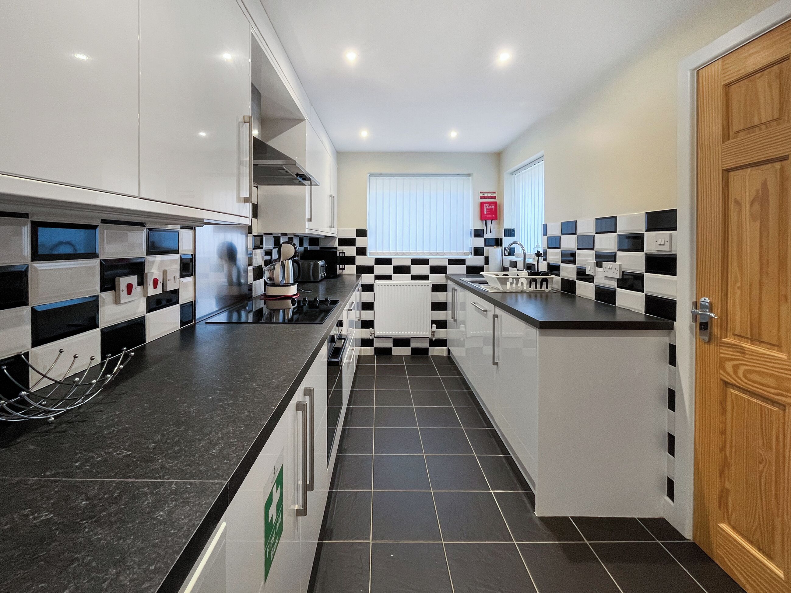 A modern kitchen with black and white checkered tiles, stainless steel appliances, and a wooden door.