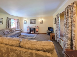 A living room with a fireplace, sofa, television, and floral curtains. - East Challoch Farm Dairy Cottage (Stranraer)