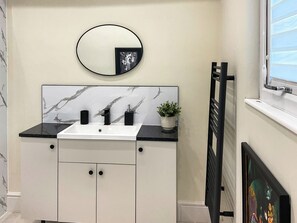 A bathroom with a white vanity, black countertop, a round mirror, and a potted plant.