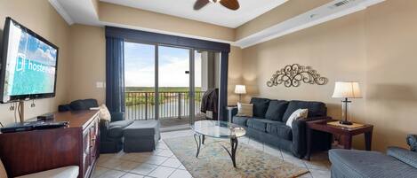 A hotel room with a balcony, a television, a sofa, a coffee table, and a ceiling fan.