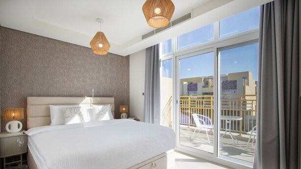 Une chambre d’hôtel moderne avec un grand lit, des lampes de chevet, une vue sur le balcon et un panorama sur la ville à travers les fenêtres.