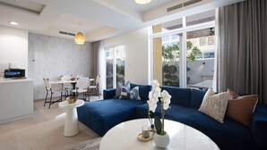 Un salon moderne avec un canapé bleu, une table basse ronde et un coin repas comprenant une table et des chaises blanches.