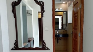A hallway with a large ornate mirror, a wooden door, and a bathroom visible in the background.