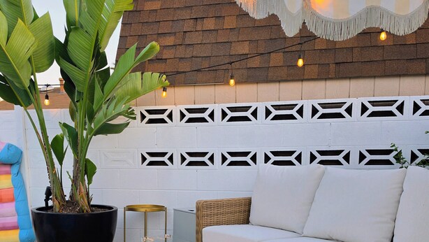 Un área junto a la piscina con un sofá blanco para exteriores, una chimenea, una planta en maceta y una pared con diseño.
