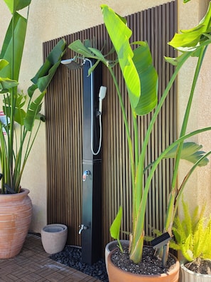 A modern outdoor shower area with a vertical wooden panel backdrop, surrounded by potted plants.