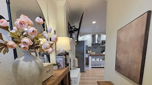 Un pasillo con un banco de madera, un jarrón con flores, una lámpara y un cuadro en la pared.