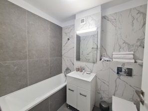 Een moderne badkamer met een bad, een wastafel met spiegel en marmeren wanden.