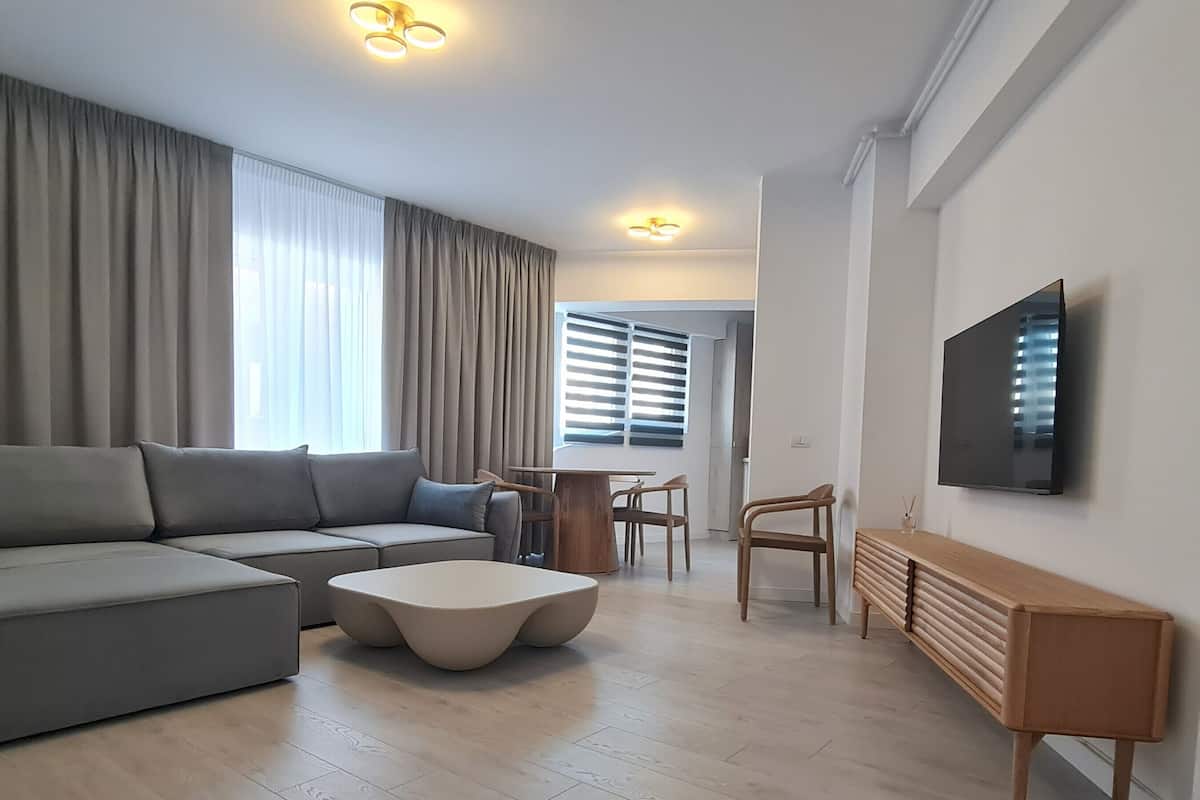 A modern living room with a grey sectional sofa, a round coffee table, and a TV mounted on the wall.