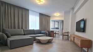 Moderni olohuone, jossa on harmaa kulmasohva, pyöreä sohvapöytä ja seinälle asennettu televisio.