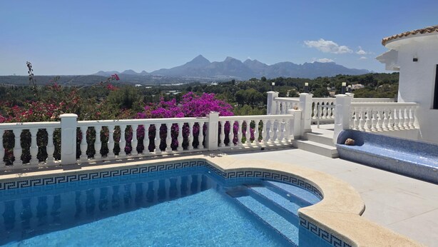 Una piscina con vistas a montañas, rodeada de barandillas blancas y un edificio blanco.