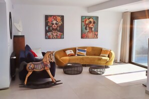 Ein modernes Wohnzimmer mit einem gelben Sofa, zwei Gemälden, einem hölzernen Schaukelpferd und einem großen Fenster.