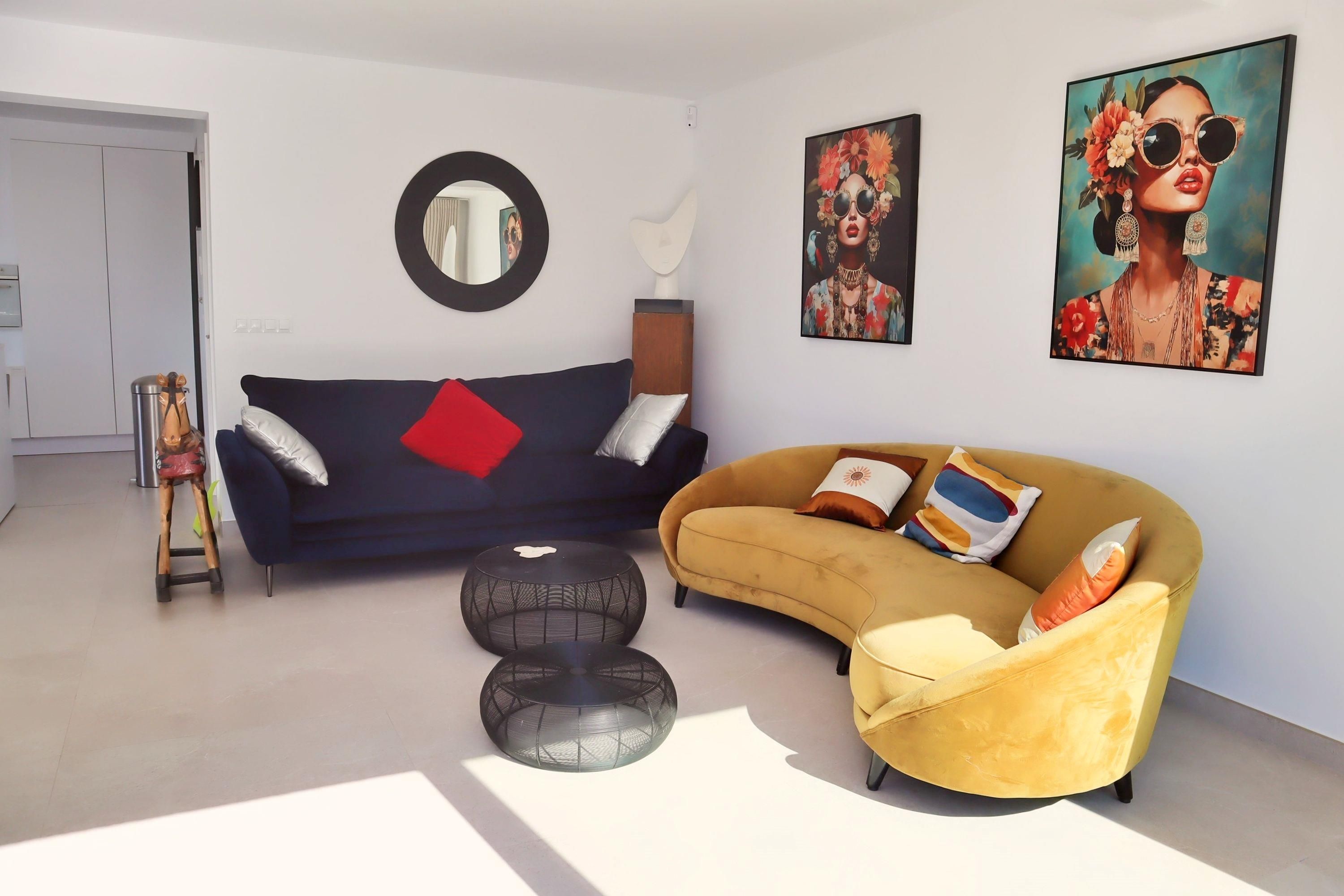 Una sala moderna con un sofá azul oscuro, un sillón amarillo y dos otomanas negras redondas.