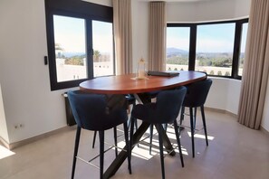 Ein Essbereich mit einem runden Tisch und vier Stühlen, großen Fenstern mit Vorhängen und Blick auf die Landschaft.