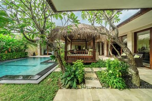 Un espace aménagé au bord de la piscine, comprenant un gazebo à toit de chaume, une chaise longue et un coin repas offrant une vue sur la piscine.