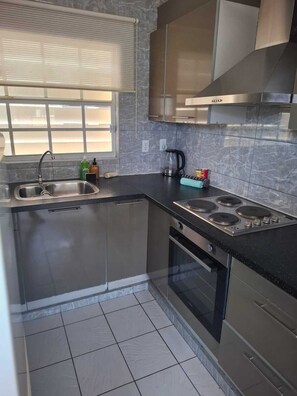 A modern kitchen with stainless steel appliances, a window with blinds, and a tiled backsplash. - Casa Andries – Centrally Located and Comfortable in Curaçao   (Willemstad)