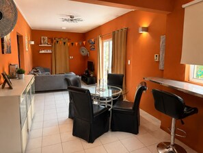 A modern living room with a sofa, a glass-top dining table, and black chairs. - Casa Andries – Centrally Located and Comfortable in Curaçao   (Willemstad)
