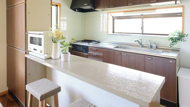 Een moderne keuken met houten kastjes, een wit aanrecht, twee krukken en een raam voor natuurlijk licht.