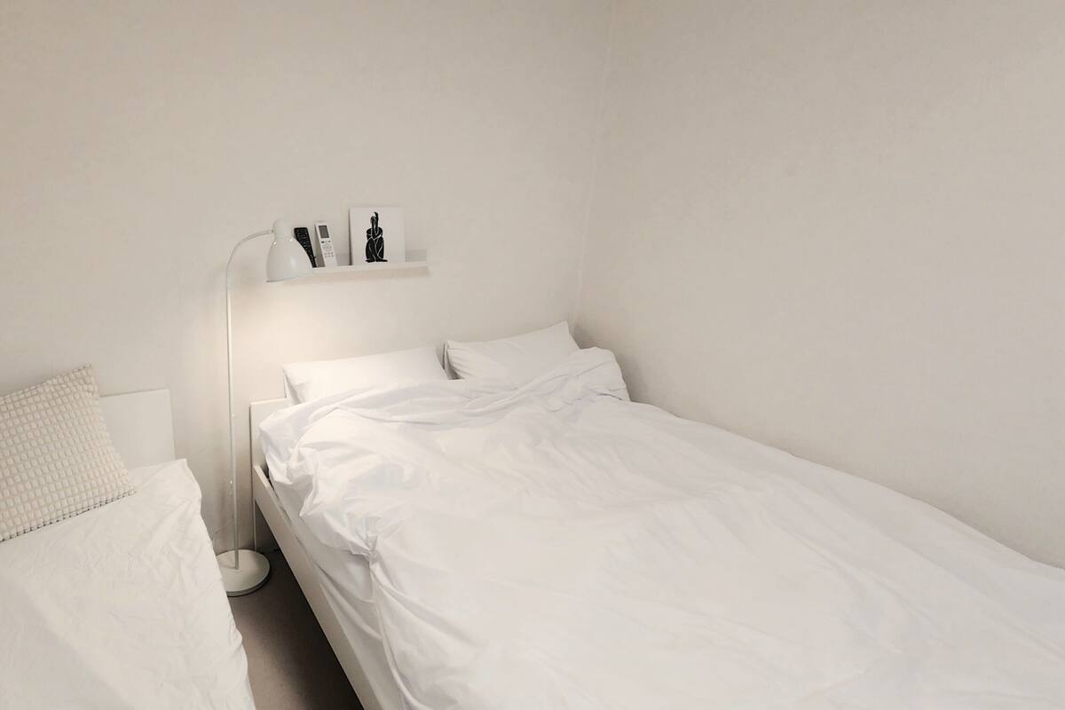 A single bed with white bedding, a bedside lamp, and a shelf with a few items.