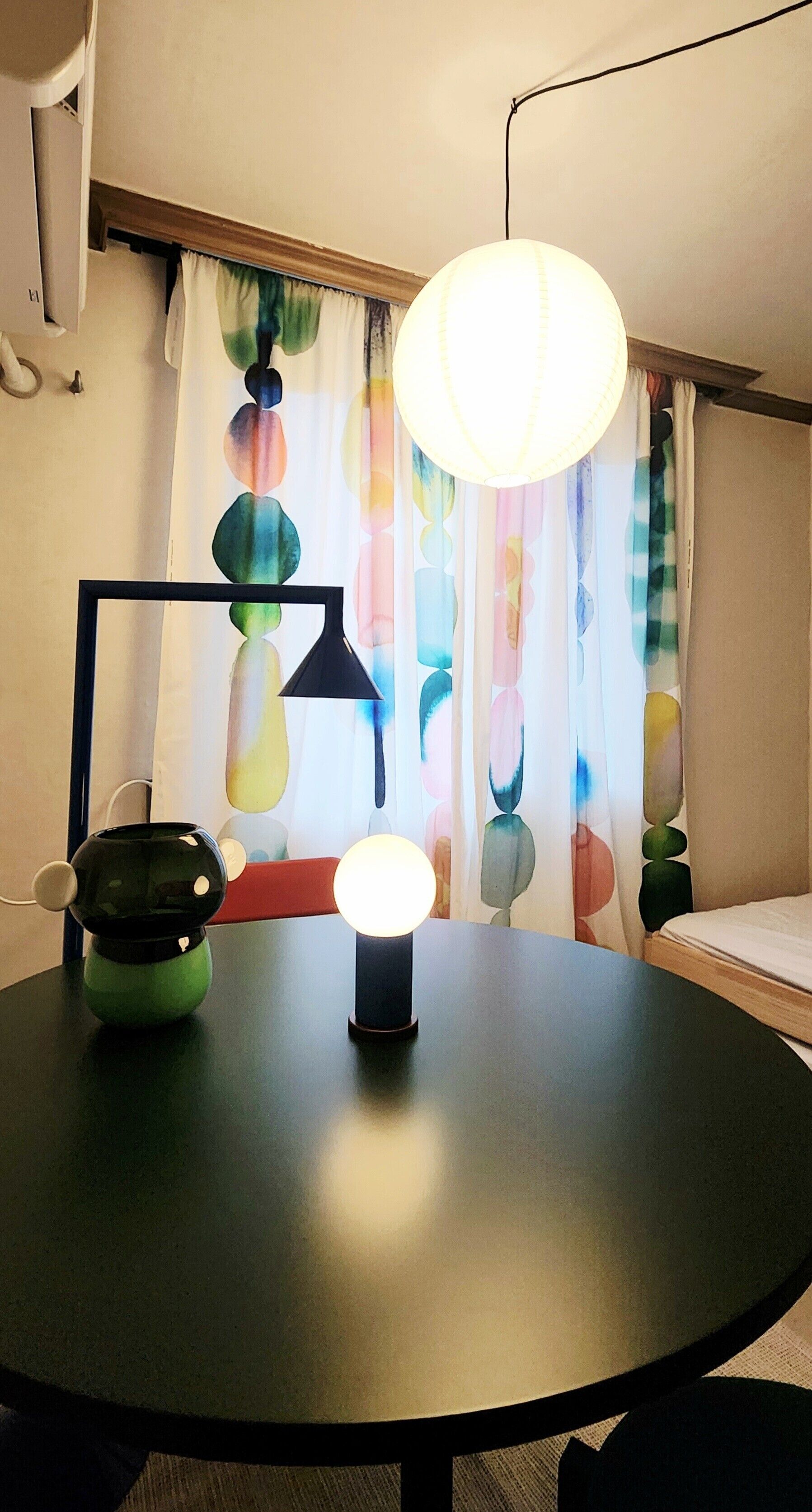 A round table with a lamp, a decorative object, and a curtain with a colorful pattern.