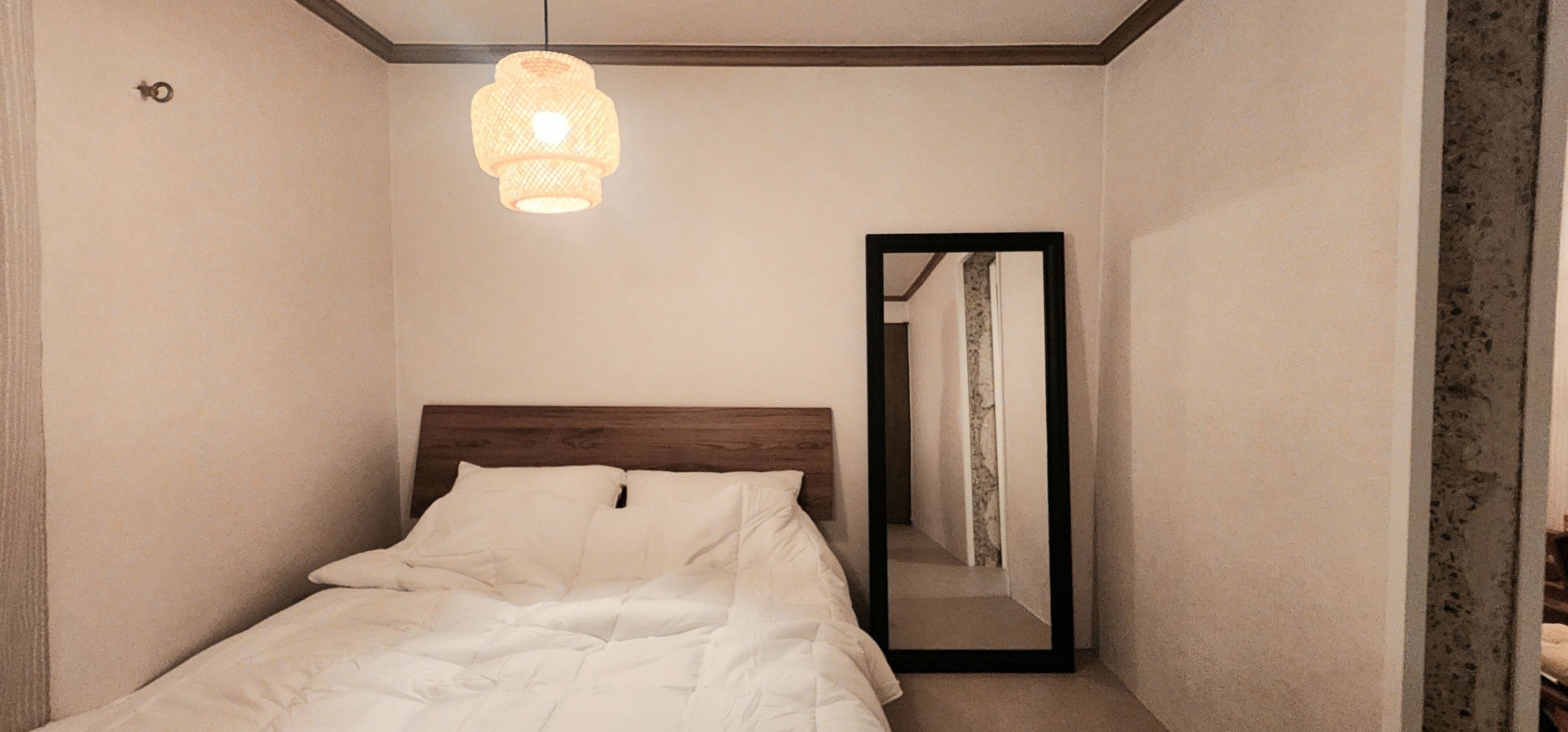 A bedroom with a bed, a hanging light fixture, and a mirror reflecting a door.