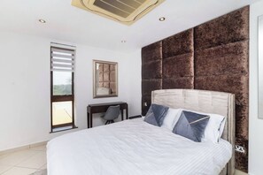 A bedroom with a large bed, a desk, and a window with blinds. - Modern 3bdr Apt at Villaggio - Rooftop Pool & Skybar (Accra)