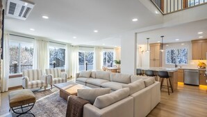 A spacious living room with a large beige sectional sofa, a coffee table, and a patterned rug. There is a kitchen area with wooden cabinets and a dining table with chairs. - Cle Elum Sunrise Lodge (Cle Elum)