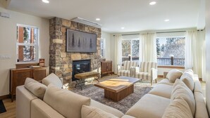 A living room with a stone fireplace, a large sofa, a coffee table, and a view of the outdoors through large windows. - Cle Elum Sunrise Lodge (Cle Elum)