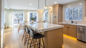A modern kitchen with a central island, bar stools, and a large window with a view of snow-covered trees. - Cle Elum Sunrise Lodge (Cle Elum)