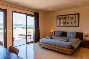 A bedroom with a large bed, a dining table, and a view of the outdoors through a sliding door. - VILLA Edén Mediterráneo – Your Private Retreat in Ibiza Weekly Villas (Ibiza)
