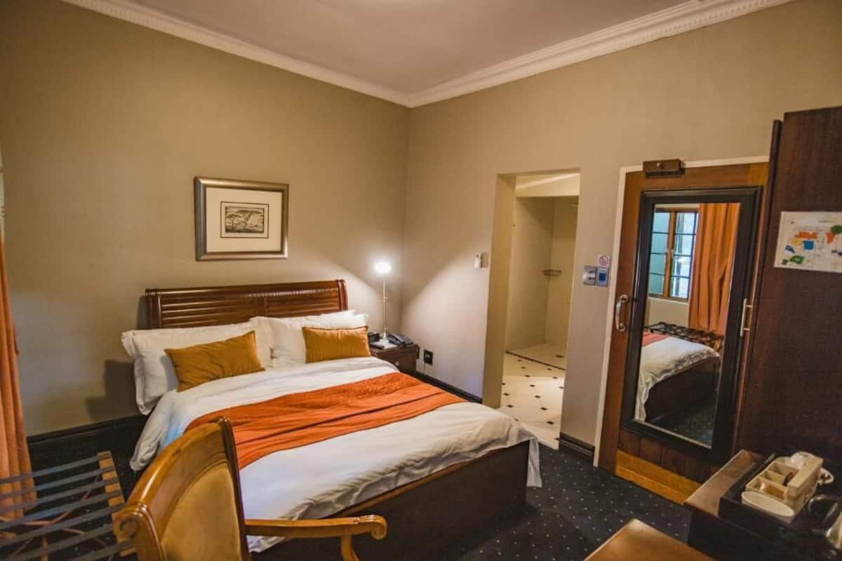 A hotel room with a bed, bedside table, lamp, and a mirror.