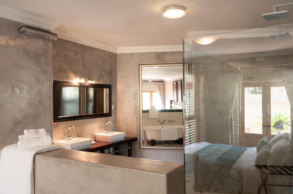 A modern bathroom with a large mirror, two sinks, a shower, and a bed with towels.