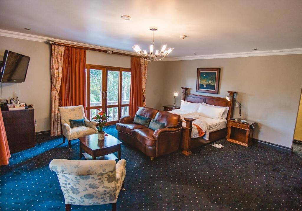 A hotel room with a large window, a sofa, a chair, a bed, a desk, and a television.