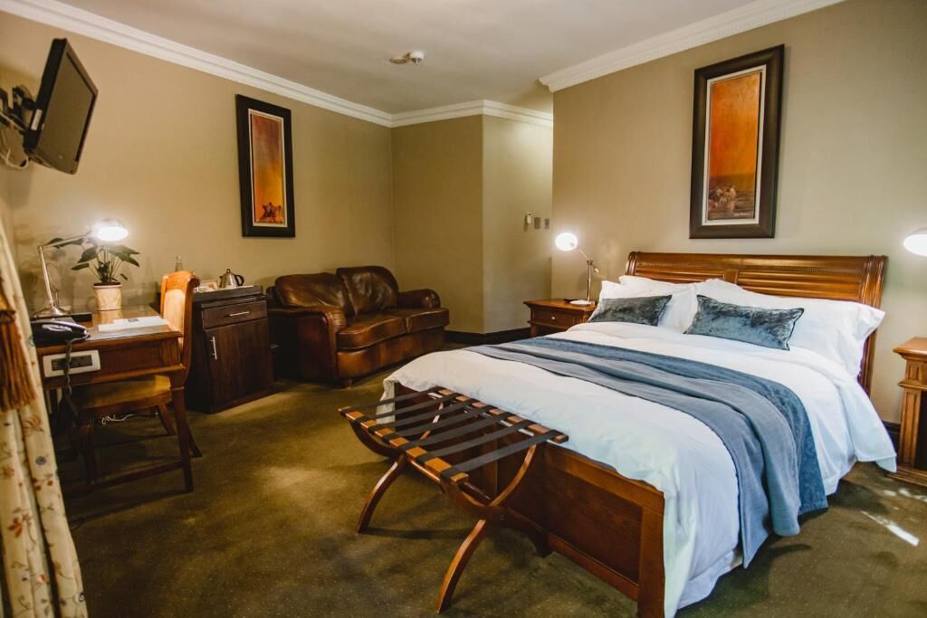 A hotel room with a bed, a desk, a chair, a lamp, and a framed picture on the wall.