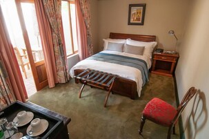 A hotel room with a bed, bedside table, chair, and a window with curtains.